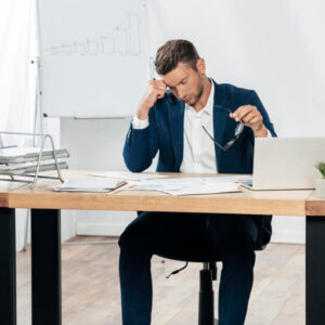 یک مدیر ارشد‌ دارای استرس‌ پشت میز کارش با نمودارهایی که نمادی از سیستم مدیریت عملکرد منابع انسانی است.